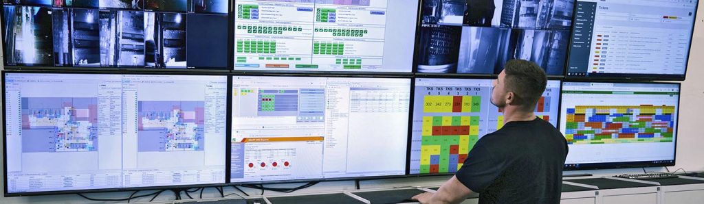 Large wall of control‑room monitors displaying real‑time warehouse performance, system status, and automation insights to support fast decision‑making and optimized distribution center operations.