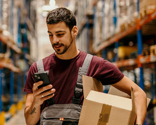 warehouse worker using a mobile phone to access real‑time information and manage tasks within a modern distribution center.