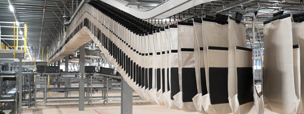 wide view of an automated pocket conveyor system transporting hanging and flat goods efficiently through a distribution center showcasing high throughput sequencing capabilities and scalable omnichannel fulfillment performance.