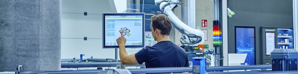 Man in a warehouse reviewing a digital pharmacy‑automation dashboard on a screen, highlighting accurate dispensing, streamlined workflows, and space‑efficient automation for modern healthcare fulfillment.
