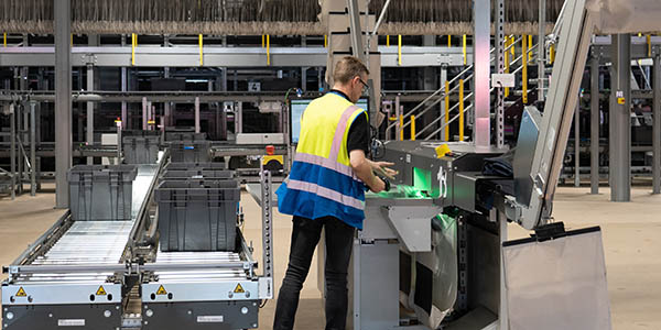 Worker in a yellow safety vest performing tasks in a KNAPP‑enabled area of the distribution center, highlighting safe, efficient, and sustainability‑focused warehouse operations.