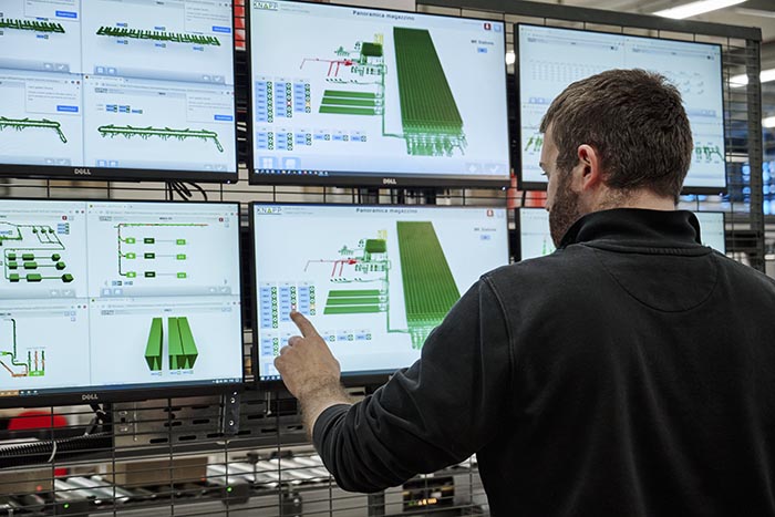Image of a warehouse worker using a multi‑monitor software control station, showing advanced KNAPP system interfaces that provide real‑time visibility, workflow coordination, and efficient management of automated fulfillment processes.